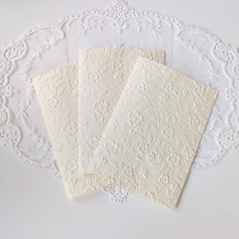Shows the ivory embossed cards on their own. Front of the card is fully embossed with the floral vine design, creating a textured appearance. Inside of the card shows one blank page for writing the message.