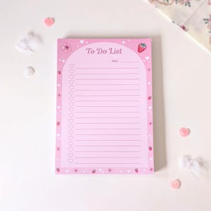 Op de afbeelding: Een roze To Do List notitieblok met een aardbeien- en bloemenrand. Het notitieblok heeft een koptekst met "To Do List" en een ruimte voor de datum. Het notitieblok is versierd met hartjes en aardbeien.