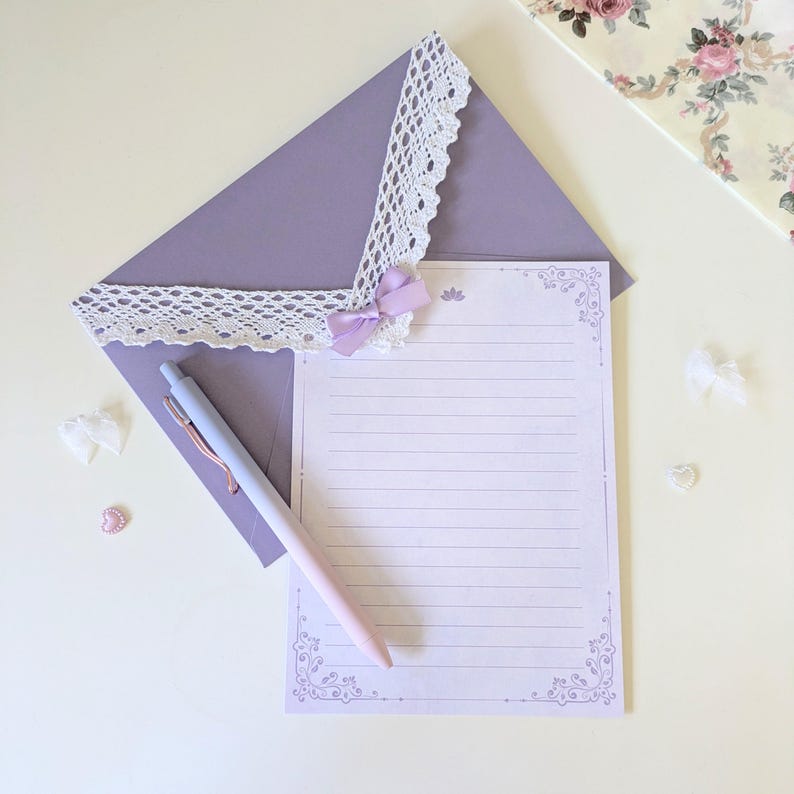 May include: A purple envelope with a white lace trim and a lavender bow. A white lined sheet of paper with a decorative border is inside the envelope. A blue and pink pen is lying on top of the envelope.