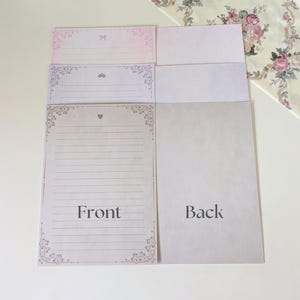 May include: A set of three stationery note cards with decorative borders. The front of the cards feature a pink, purple, and white color scheme with floral designs. The back of the cards are blank. The text "Front" and "Back" is printed on the cards.