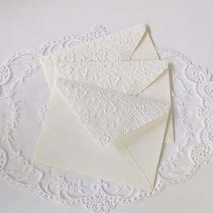 Shows the ivory embossed envelopes in detail. Each envelope flap is embossed with a floral vine texture.
