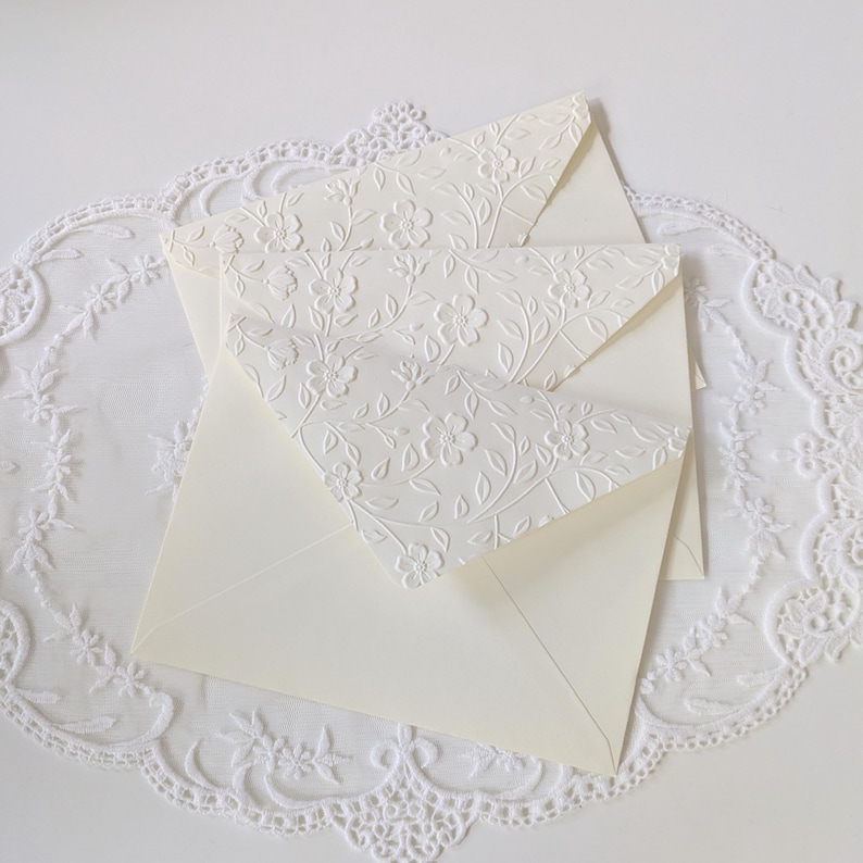 Shows the ivory embossed envelopes in detail. Each envelope flap is embossed with a floral vine texture.