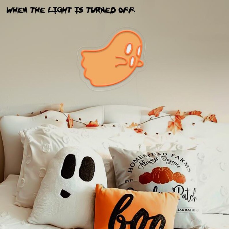 May include: A white bed with white pillows and a white ghost pillow. The pillows have a fall theme with a pillow that says "Homestead Farms Always Organic" and a pillow that says "Boo" with a pumpkin design. There is a ghost sticker on the wall behind the bed.