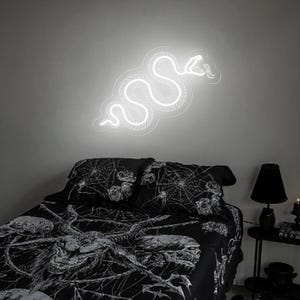 May include: A white neon snake sign on a gray wall above a black bed with a spiderweb and rose print bedding.