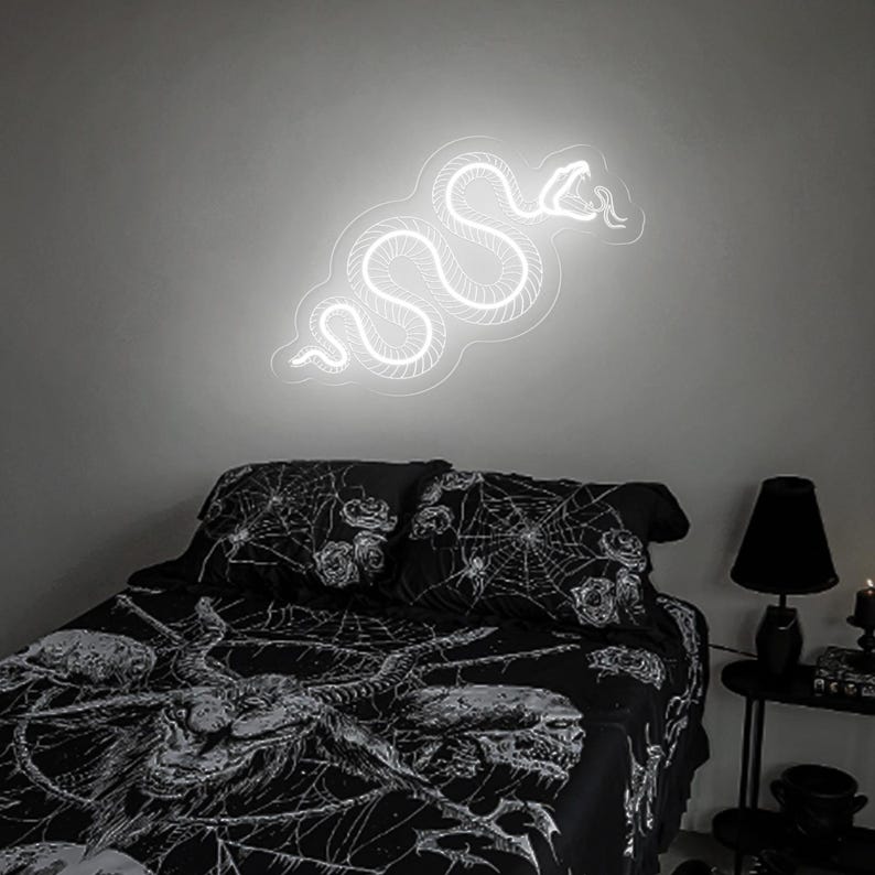 May include: A white neon snake sign on a gray wall above a black bed with a spiderweb and rose print bedding.