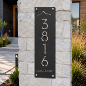 May include: A vertical rectangular black metal house address sign featuring a laser-cut mountain silhouette at the top, the numbers 3816 stacked vertically in the center, and the text CEDAR COURT at the bottom, secured with four silver corner bolts.