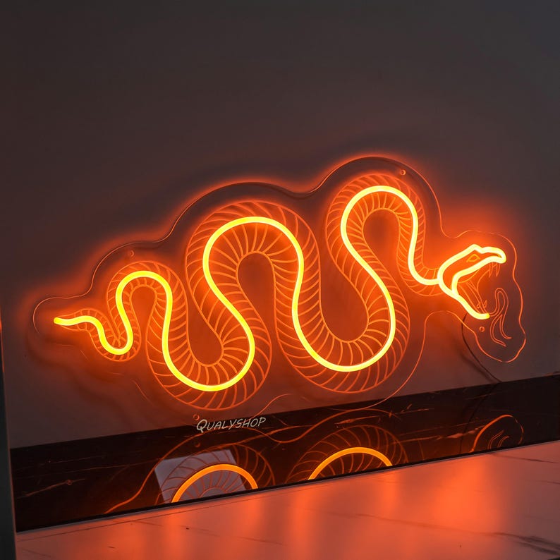 May include: A neon sign shaped like a snake with a bright orange glow. The snake is coiled and has a detailed design. The sign is mounted on a black surface.