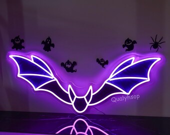 May include: Purple neon bat sign with wings spread wide. The sign is lit up and has a white outline. The sign is hanging on a wall with a black background. The text "Qualyhsop" is visible in the bottom right corner of the image.