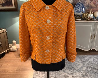 Könnte beinhalten: Orangefarbene Vintage-Jacke mit strukturiertem, wellenförmigem Muster. Sie hat einen runden Kragen, Dreiviertelärmel und glitzernde Knöpfe. Die Jacke wird auf einer schwarzen Schaufensterpuppe präsentiert. Maße in Zentimetern.