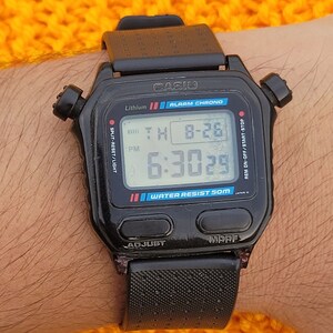 Puede incluir: Un reloj digital Casio negro con una correa negra. La esfera del reloj muestra la hora, la fecha y el d&iacute;a de la semana. El reloj es resistente al agua hasta 50 metros. El reloj tiene un bot&oacute;n split-reset/light, un bot&oacute;n rem on-off/start-stop y un bot&oacute;n adjust.