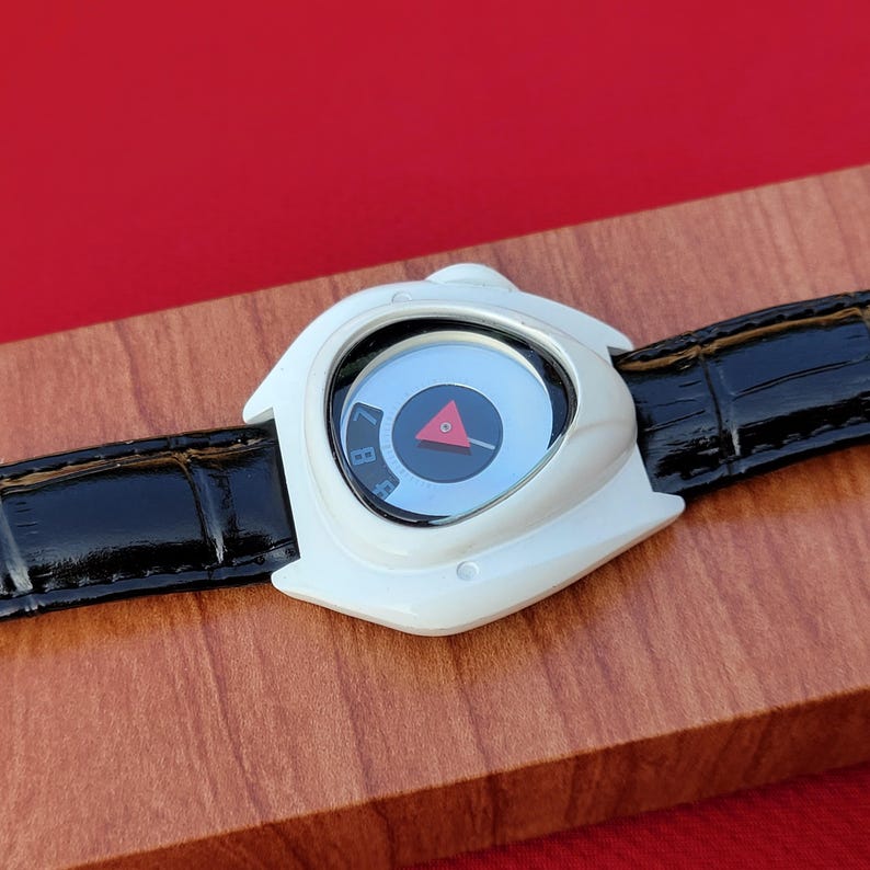 Puede incluir: Reloj de pulsera blanco con una correa de cuero negro. La esfera del reloj es azul claro con un tri&aacute;ngulo rojo y marcas negras. El reloj tiene un dise&ntilde;o angular &uacute;nico.