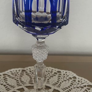 Puede incluir: Una copa de vino de cristal azul cobalto con un patrón de corte decorativo. El tallo presenta un diseño en forma de diamante. La copa se apoya sobre un tapete de encaje blanco. Una pieza hermosa.