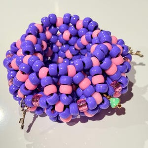May include: A purple and pink beaded bracelet with charms, including keys and a mushroom. The bracelet is made of small, round beads and is coiled into a circular shape.