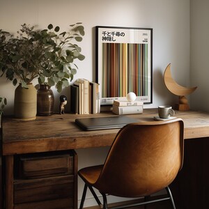 May include: A wooden desk with a leather chair, a laptop, and a framed poster with Japanese text. The desk also features a vase with greenery, books, a small figurine, and a decorative wooden crescent moon.