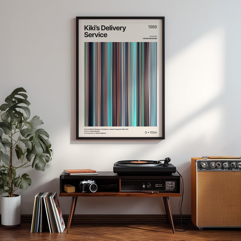 May include: A framed poster with the text "Kiki's Delivery Service" and a colorful vertical stripe design. The poster is displayed above a mid-century modern style console with a record player, camera, and records.