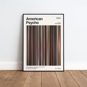 May include: A framed film poster for the 2000 movie American Psycho, directed by Mary Harron. The design features a central vertical colour palette of brown, grey, and black stripes, with the title, year, and film credits printed in black text.