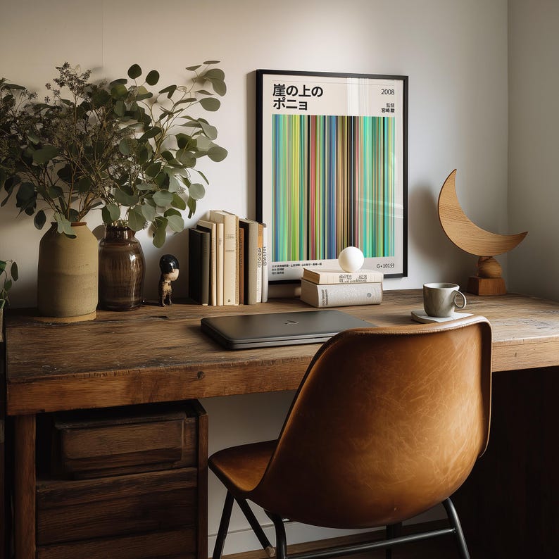 May include: A wooden desk with a framed poster featuring Japanese text and colorful vertical stripes. A laptop, books, and a small sculpture are on the desk. A leather chair is in front of the desk, and a vase with greenery is on the left.