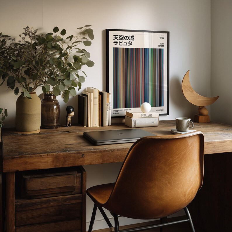 May include: A wooden desk with a framed poster featuring Japanese text and colorful vertical lines. A brown leather chair sits in front of the desk. Other items include books, a laptop, vases with greenery, and a decorative wooden crescent.