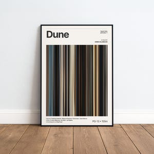 Puede incluir: Un póster de película enmarcado para el filme Dune de 2021, que muestra el título, el año de estreno, el director Denis Villeneuve, los nombres del reparto y los créditos técnicos. El gráfico central consiste en franjas verticales de colores marrón, negro y azul.