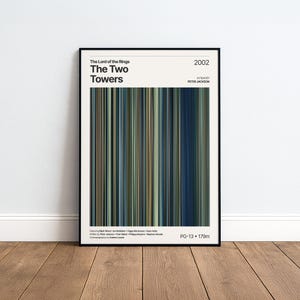 May include: A framed poster for "The Lord of the Rings: The Two Towers" film. The poster has a black frame and a vertical striped design in shades of blue, green, and brown. The film's title, year, and director are displayed at the top.