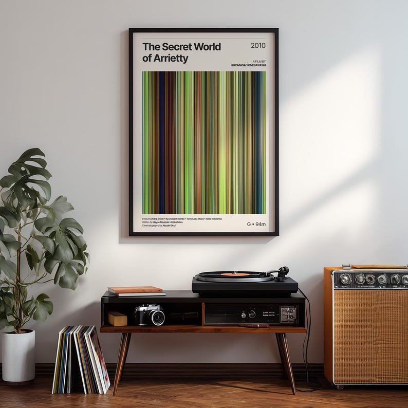 May include: A framed poster for "The Secret World of Arrietty" movie, featuring a colorful vertical stripe design. The poster is displayed above a mid-century modern style record player console with a turntable, camera, and amplifier.