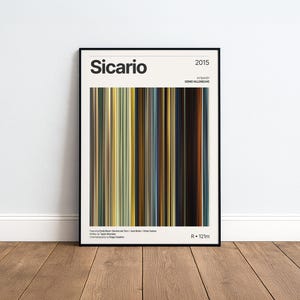 Könnte beinhalten: Ein gerahmtes Filmplakat für den Film Sicario aus dem Jahr 2015, unter der Regie von Denis Villeneuve. Das Design zeigt eine zentrale vertikale Strichcode-Grafik aus dünnen, mehrfarbigen Streifen in Gelb-, Braun-, Blau- und Schwarztönen mit Text.
