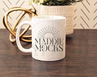 May include: White ceramic mug with a black and white graphic design of a sun with rays and the text "Maddie Mocks".