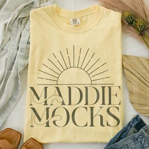 May include: A yellow t-shirt with a graphic design of a sun with rays and the text "MADDIE MOCKS" in black.