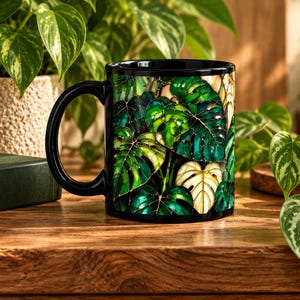 May include: A black ceramic mug featuring a vibrant, stained-glass style print of overlapping monstera leaves in shades of deep emerald, forest green, and cream. The design wraps around the exterior, showcasing intricate dark outlines.