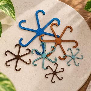 May include: A collection of six flat, star-shaped hooks with six curved arms each, arranged in various sizes and colors including blue, brown, and teal. These decorative items feature a smooth, matte finish and are crafted with a central hub.