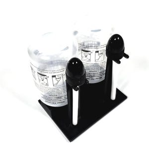 May include: Two clear plastic bottles with black caps and white tubes attached to a black plastic stand. The bottles have instructions printed on them that say "Water Fill Level" and "WARNING".