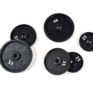 Peut inclure: Cinq plaques de poids noires avec des chiffres blancs. Les plaques pèsent 45, 35, 25, 25 et 45 livres.
