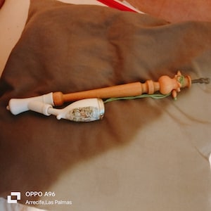 Könnte beinhalten: Eine Holzpfeife mit einem Keramikkopf, der mit einer Waldlandschaft verziert ist. Die Pfeife hat einen braunen Holzstiel mit einer geschnitzten Holzfigur am Ende. Die Pfeife liegt auf einer braunen Stoffoberfläche.