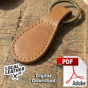 May include: A handcrafted, light brown leather keychain with a brass ring. The keychain is stitched with a contrasting thread and features the text "Digital Download" and the Local Leather Co. logo.