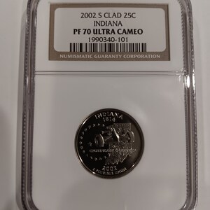 Może przedstawiać: Moneta ćwierćdolarowa Indiana z 2002 roku, zamknięta w przezroczystym etui ochronnym. Moneta zawiera napis "INDIANA 1816" i "CROSSROADS OF AMERICA". Etui zawiera etykietę z takimi szczegółami jak "PF 70 ULTRA CAMEO".
