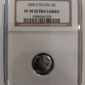 Peut inclure: Une pièce de monnaie en argent 2000 S 10C, classée PF 70 Ultra Cameo, dans un boîtier de protection transparent. La pièce représente un profil de personne et l'année 2000. Le boîtier porte l'inscription "NUMISMATIC GUARANTY CORPORATION".