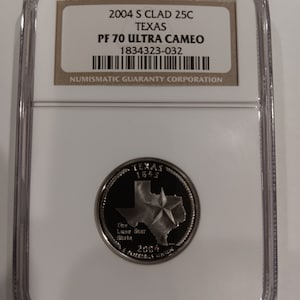 Peut inclure: Une pièce de monnaie de 25 cents du Texas de 2004, dans un étui de protection transparent. La pièce présente le contour de l'État et une étoile. L'étui porte une étiquette avec des détails, dont "PF 70 ULTRA CAMEO".