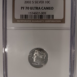 Peut inclure: Une pièce de monnaie en argent 2002 S 10C, classée PF 70 Ultra Cameo, dans un boîtier de protection transparent. La pièce représente un profil d'une personne et le mot "LIBERTY". Le boîtier comprend le texte "NUMISMATIC GUARANTY CORPORATION".