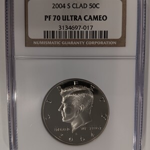 Peut inclure: Une pièce de monnaie argentée 2004 S Clad 50C, classée PF 70 Ultra Cameo, dans un boîtier de protection transparent. La pièce représente un profil d'homme et le texte "IN GOD WE TRUST". Le boîtier porte une étiquette avec "NUMISMATIC GUARANTY CORPORATION".