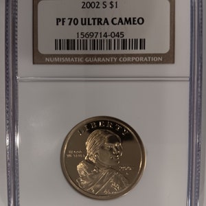 Peut inclure: Une pièce de monnaie dorée dans un boîtier en plastique transparent. La pièce représente un profil de femme et le mot "LIBERTY". Le boîtier porte une étiquette avec le texte "2002 S $1" et "PF 70 ULTRA CAMEO".
