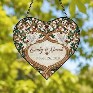 May include: Heart-shaped stained glass wedding decoration with a tree design, doves, and the names "Emily & Jacob" along with the date "October 26, 2026". The design features brown, green, red, and white colours, suspended by a black chain.