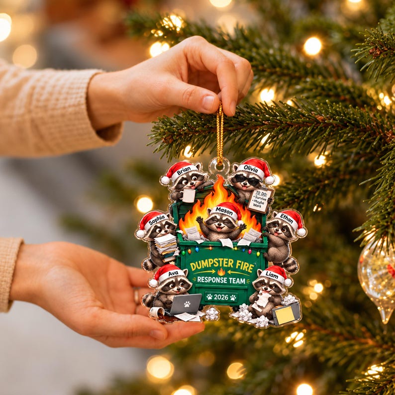 May include: A flat, acrylic Christmas ornament featuring a green dumpster with orange flames and seven raccoons wearing red Santa hats. The text reads DUMPSTER FIRE RESPONSE TEAM 2026, with individual names Brian, Olivia, Mason, Sophia, Ethan, Ava, and Liam.