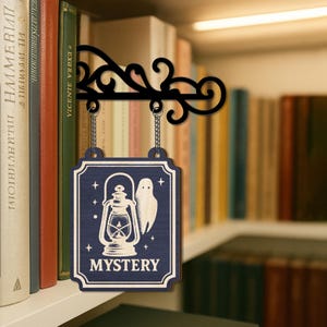 May include: A dark blue wooden sign with a white border, suspended from a black metal bracket. The sign displays a white lantern and ghost illustration, with the word "MYSTERY". The sign hangs in front of a bookshelf filled with books.