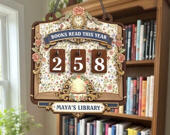 May include: Wooden sign with the text "BOOKS READ THIS YEAR" and the number "258". The sign is decorated with floral patterns, a clock, and the text "MAYA'S LIBRARY". It hangs from a chain and is displayed in front of a bookshelf.