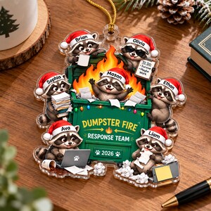 May include: A clear acrylic ornament featuring six raccoons wearing Santa hats around a green dumpster filled with orange flames. The dumpster is labeled "DUMPSTER FIRE RESPONSE TEAM" and "2026" with names Brian, Olivia, Mason, Sophia, Ethan, Ava, and Liam.