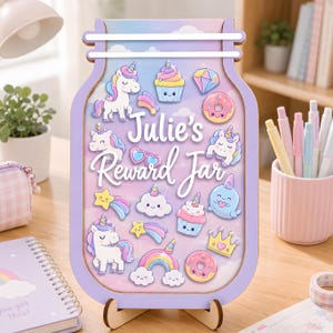 Può includere: Un barattolo premio in legno a forma di vasetto con una cornice viola chiaro. Il centro presenta uno sfondo sfumato pastello con il testo "Julie's Reward Jar" circondato da illustrazioni di unicorni, cupcake, ciambelle, nuvole e stelle.