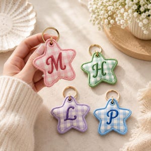 May include: Four star-shaped keychains with a gingham pattern in pink, green, purple, and blue. Each keychain features a gold-toned metal ring and a single embroidered script letter in the center, specifically the letters M, H, L, and P.