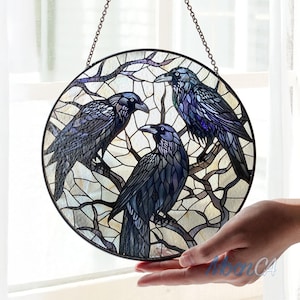 Peut inclure: Une fenêtre en verre coloré suspendue avec trois corbeaux noirs perchés sur des branches. Les corbeaux ont des plumes bleues et violettes irisées.