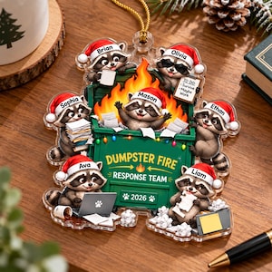 May include: A clear acrylic ornament featuring six raccoons wearing Santa hats around a green dumpster filled with orange flames. The dumpster is labeled "DUMPSTER FIRE RESPONSE TEAM" and "2026" with names Brian, Olivia, Mason, Sophia, Ethan, Ava, and Liam.