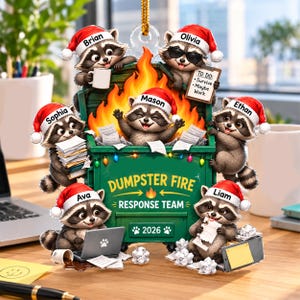 May include: A decorative ornament featuring six raccoons wearing Santa hats around a green dumpster filled with flames. The dumpster is labeled DUMPSTER FIRE RESPONSE TEAM 2026. Each raccoon is personalized with names: Brian, Olivia, Mason, Sophia, Ethan, Ava, and Liam.